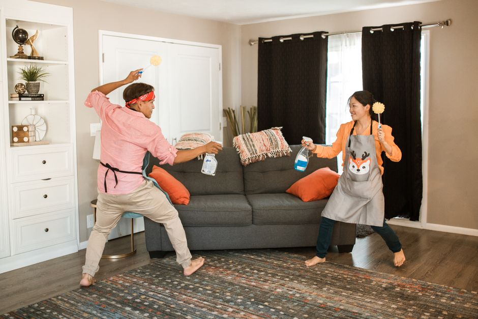 A joyful couple engages in a playful cleaning fight in their living room, showcasing light-hearted domestic life.