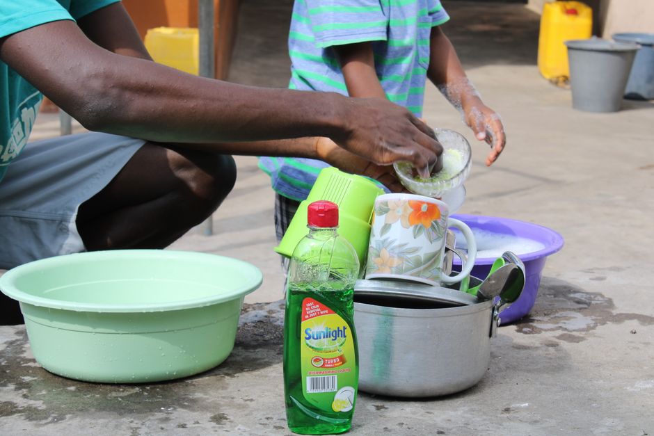 A father and child washing dishes outdoors using dishwashing liquid, combining family bonding and chores.